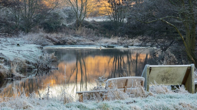 View over the frosty grass to the pond at Gibside with the reflection of an orange sky.